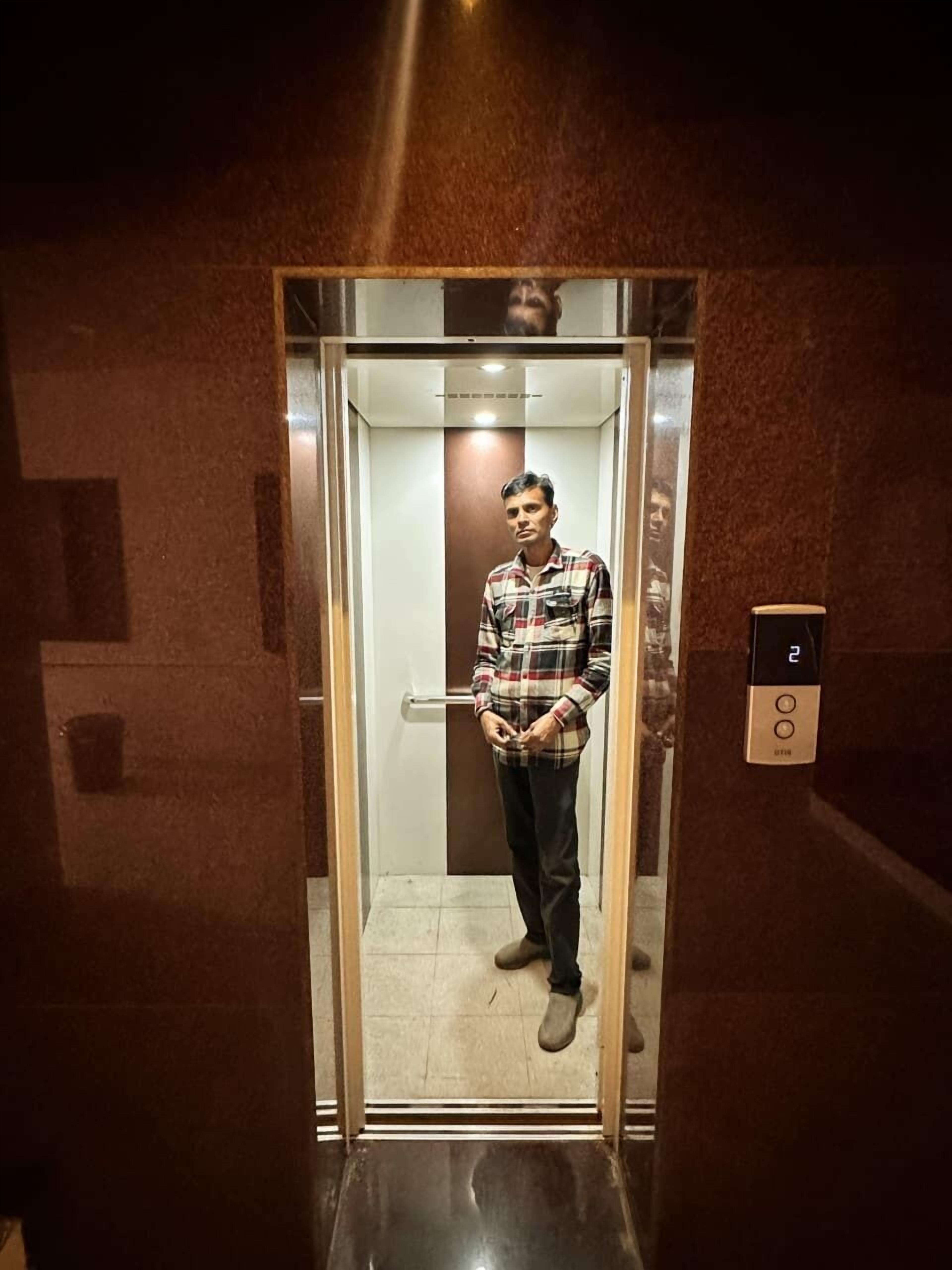 A man standing in a glass elevator door with a control panel on the right.