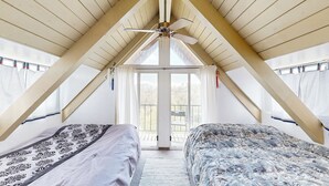 Un dormitorio con dos camas, ventilador de techo y un ventanal amplio.