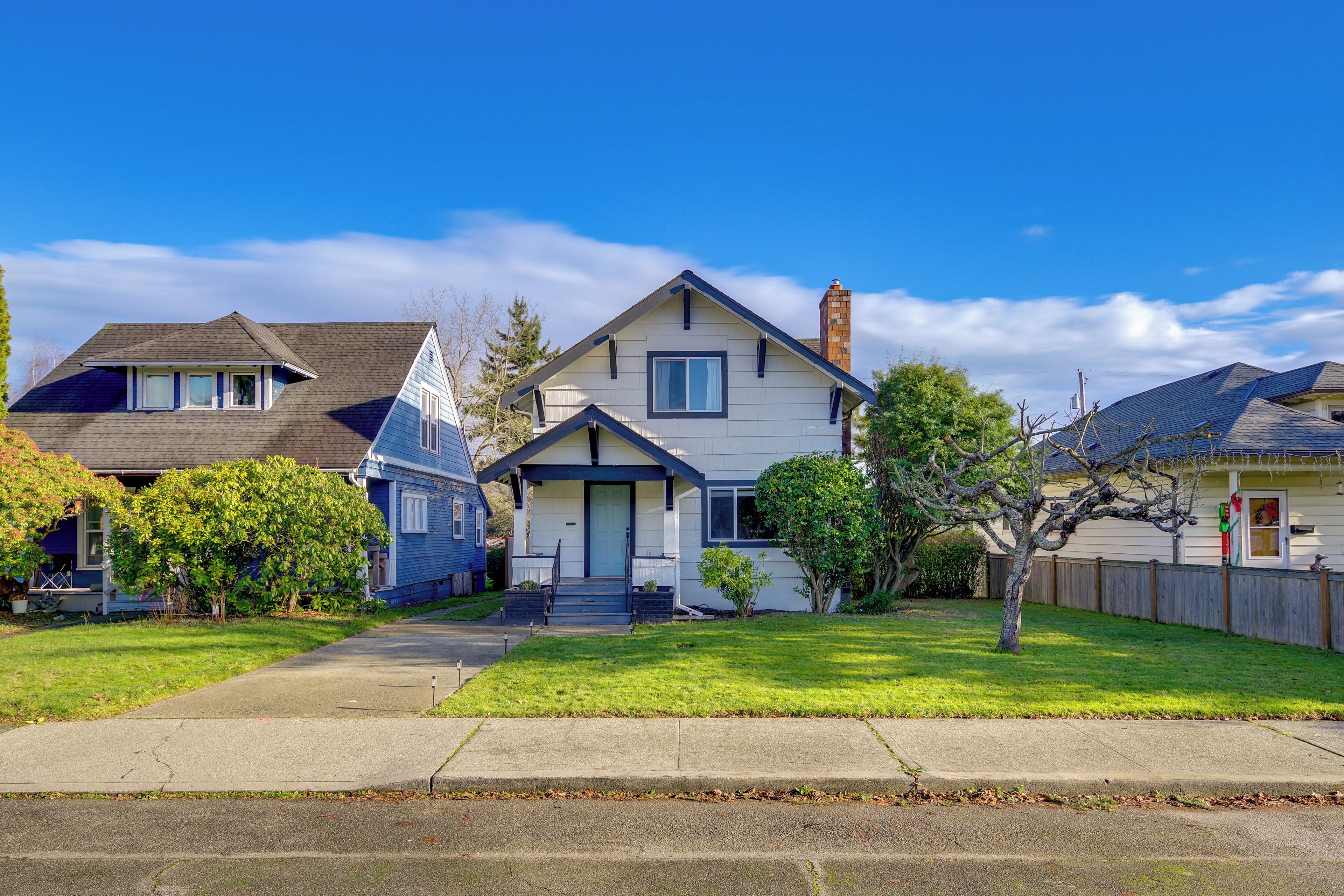 A residential street with houses, a clear sky, and a well-maintained lawn.