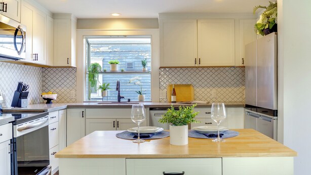 Une cuisine moderne avec des meubles blancs, un plan de travail en bois et une fenêtre agrémentée de plantes.