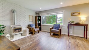 Un salon doté d’une cheminée, d’un plancher en bois, de deux fauteuils, d’une table et d’une fenêtre donnant sur un paysage verdoyant.