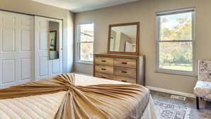 Une chambre à coucher comprenant un lit, une commode, un miroir et deux fenêtres.