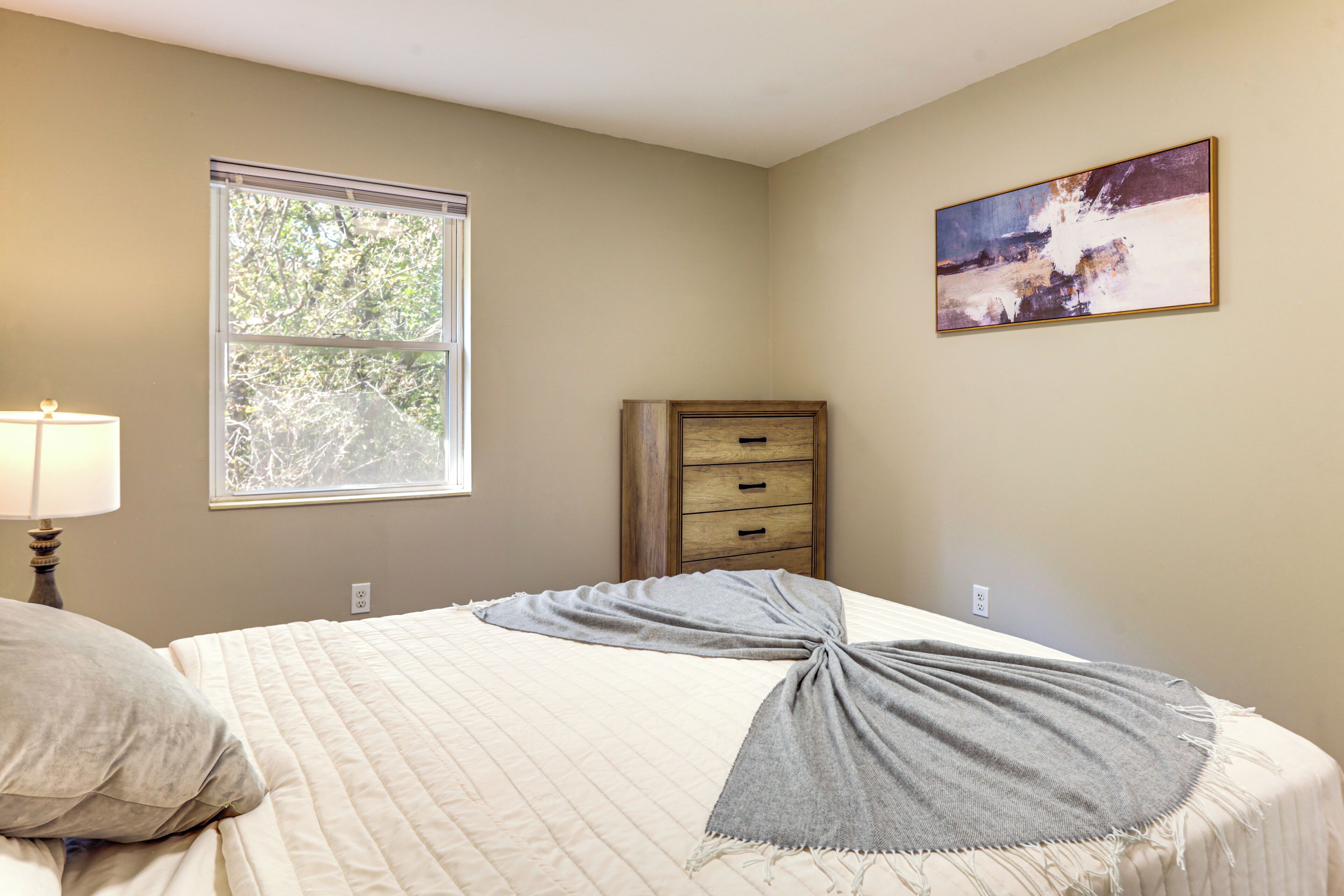 Une chambre à coucher avec un lit, une fenêtre, une commode et un tableau accroché au mur.