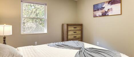 A bedroom with a bed, a window, a dresser, and a painting on the wall.