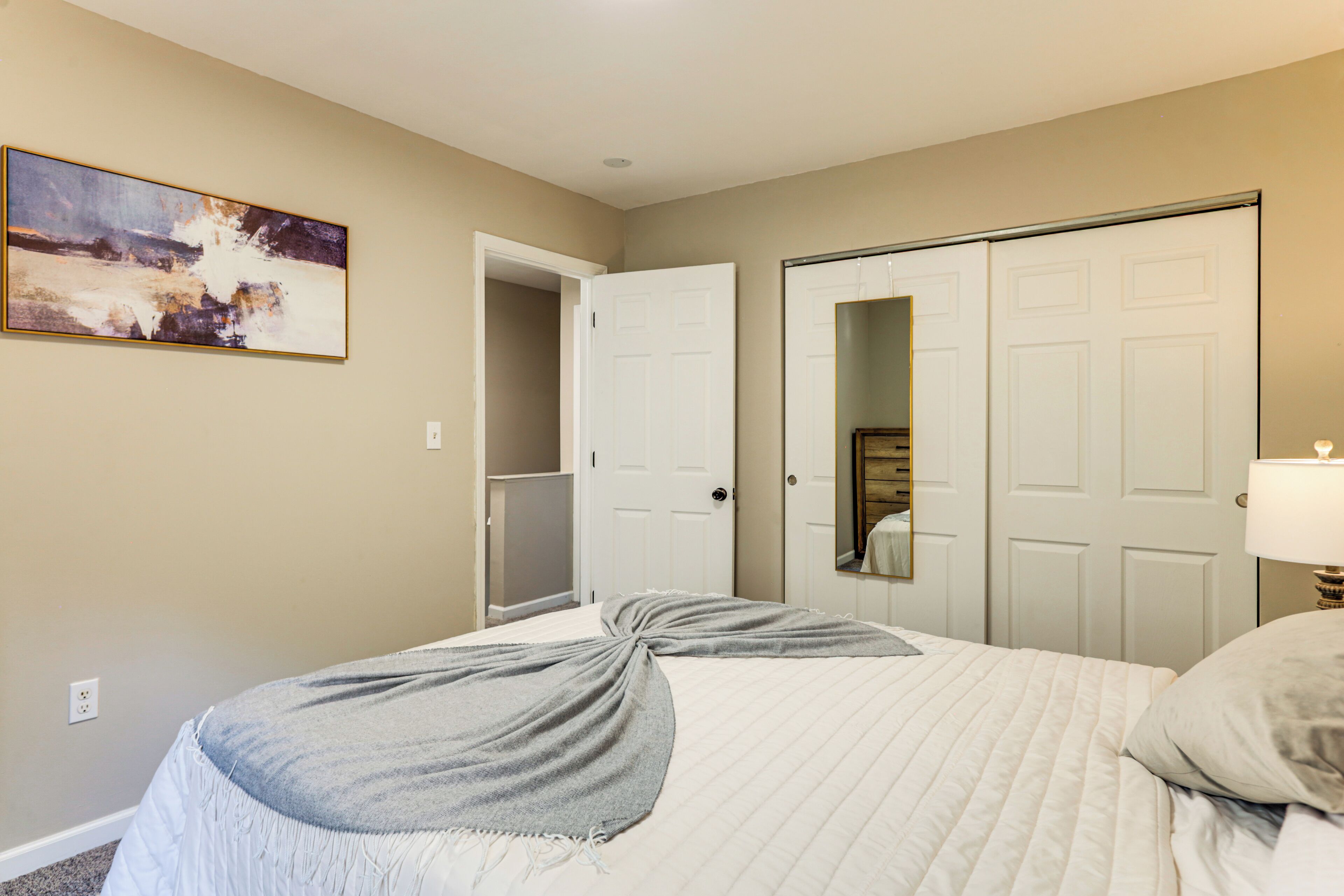 A bedroom with a bed, a door, a mirror, and a painting on the wall.