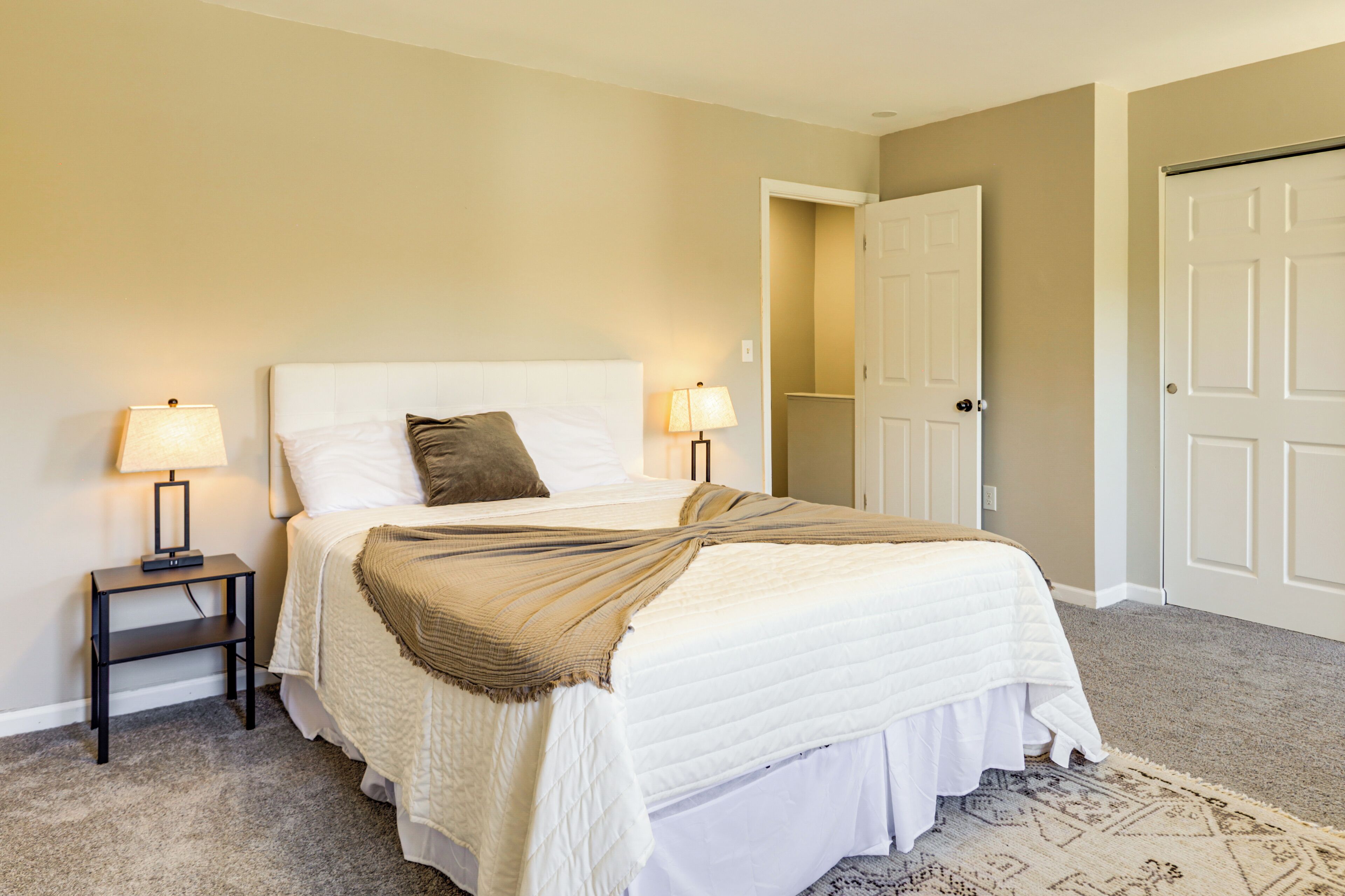 Une chambre à coucher avec un lit, deux lampes de chevet, une porte et un tapis à motifs.