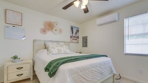 A bedroom with a bed, a nightstand, a wall calendar, a framed picture, and an air conditioning unit. - 1/2 Mi to St. Lucie River: Treasure Coast Home (Stuart)