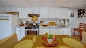 A modern kitchen with white cabinets, a stove, and a sink. There is a dining table with a placemat and a potted plant. - 5 Mi to Dtwn Riverside & Hospital! Remote-work Hub (Riverside)