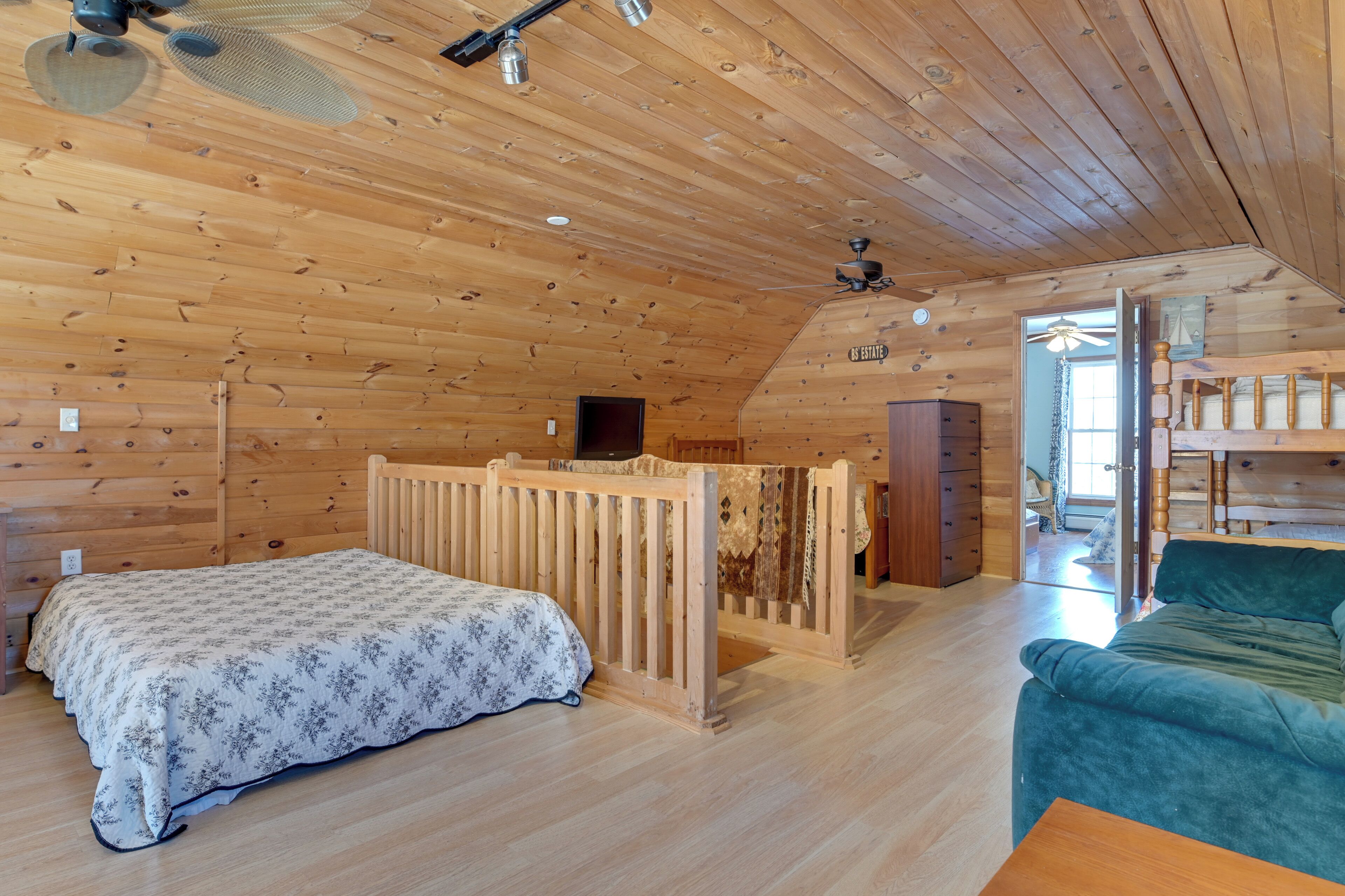 Une chambre dans une cabane en bois, avec un lit, un canapé vert, un berceau en bois et un ventilateur de plafond.