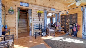Interior de una cabaña de madera con escalera, muebles de mimbre y una figura decorativa de un oso.