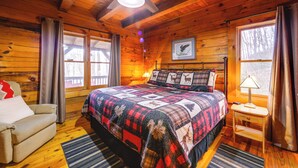 A cozy cabin bedroom with a large bed, a chair, a desk, and a ceiling fan. - Creek On-site! Cabin 7 Mi to Cataloochee Ski Area (Maggie Valley)