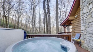 A hot tub on a wooden deck with a stone cabin in the background. - Creek On-site! Cabin 7 Mi to Cataloochee Ski Area (Maggie Valley)