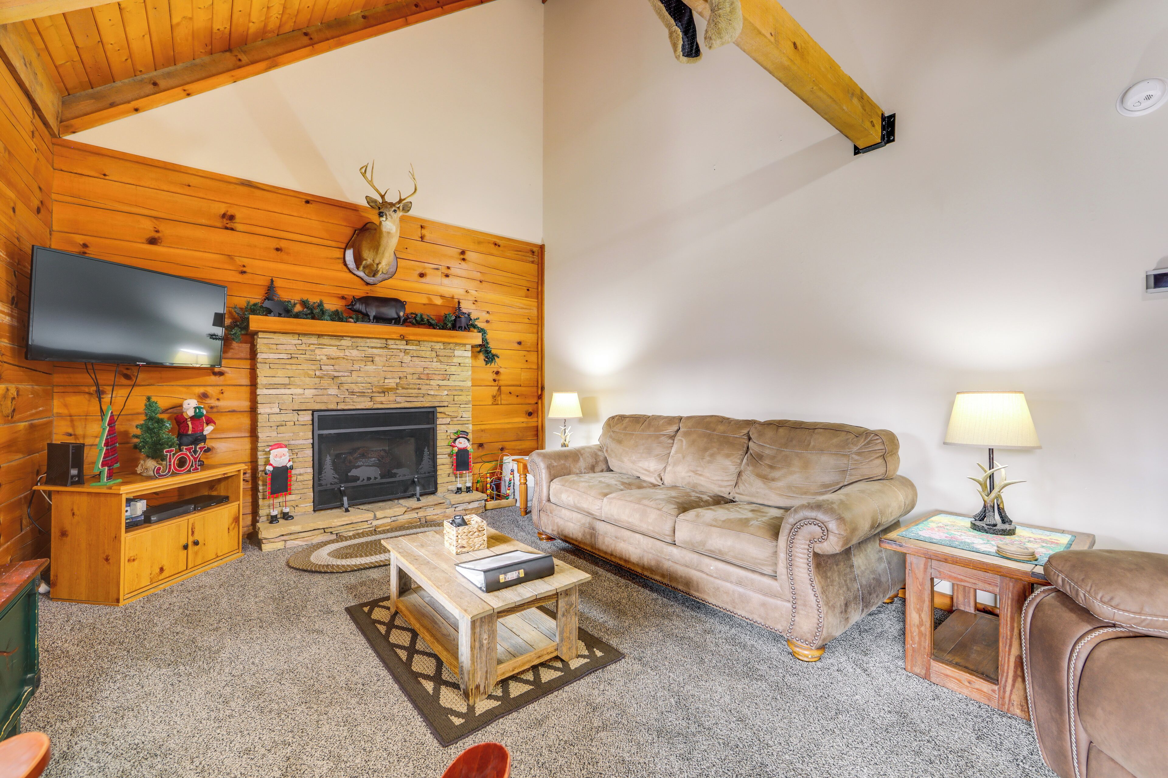 A cozy living room with a stone fireplace, wooden walls, a leather sofa, a television, and a small table with a lamp.
