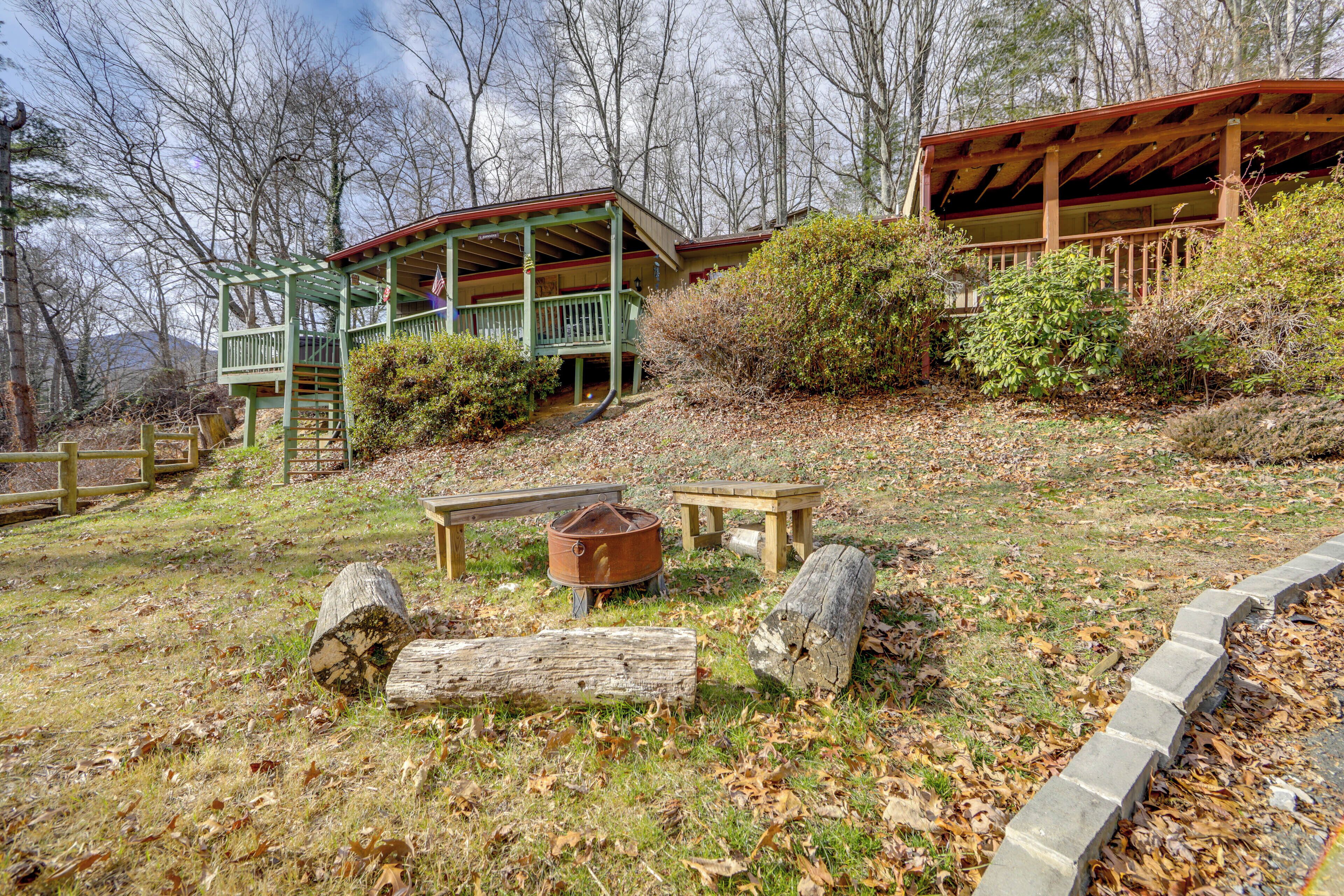 A rustic cabin with a porch, a fire pit, and a picnic table in a wooded area.