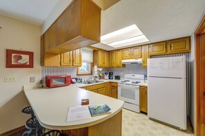 A kitchen with wooden cabinets, a white countertop, a microwave, a stove, and a refrigerator.