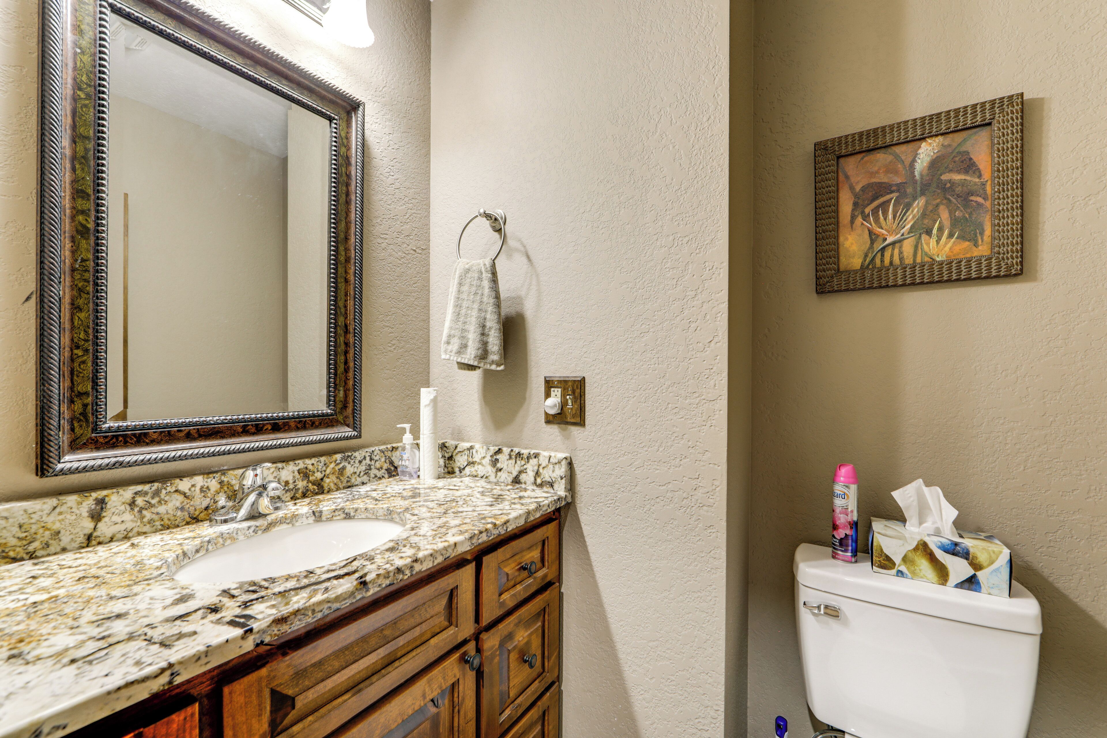 Une salle de bain avec un lavabo en marbre, des meubles en bois, un grand miroir, un porte-serviettes, des toilettes et un tableau encadré au mur.