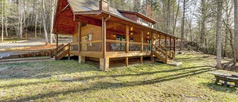 A wooden cabin with a porch and a deck, surrounded by trees.