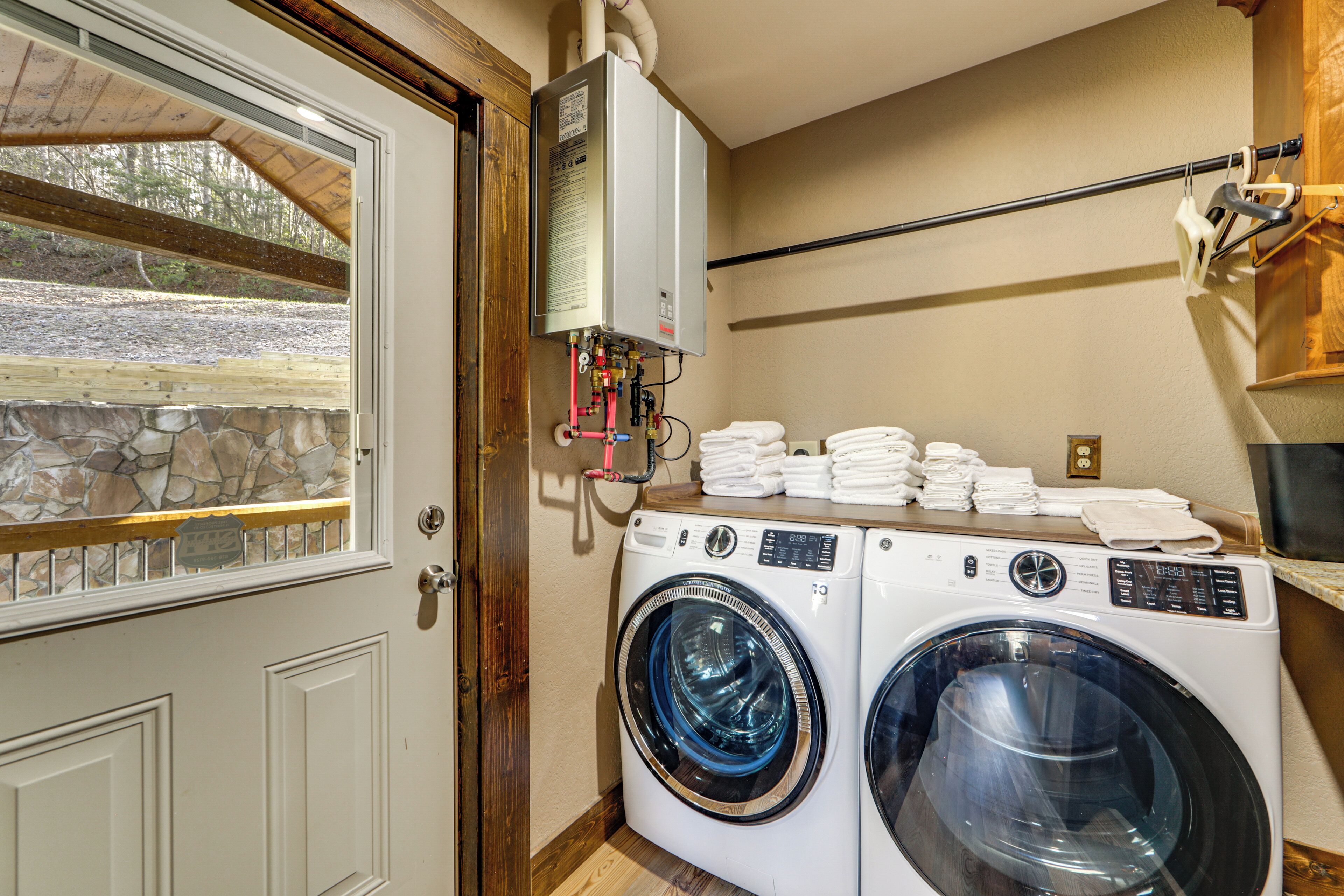 A laundry room with two front-loading washing machines, a stacked towel rack, and a water heater.