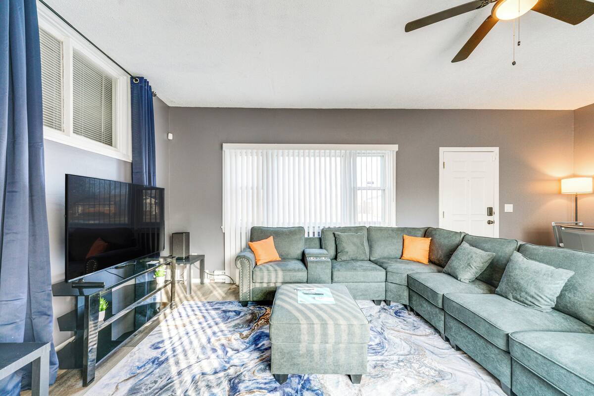 A living room with a sectional sofa, a flat-screen TV, a glass coffee table, and a patterned rug.