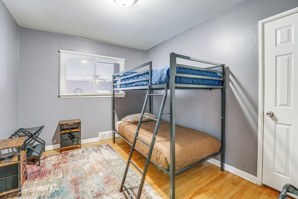 A dormitory room with bunk beds, a desk, a chair, a small table, a window with blinds, and a door. - Game, Stay & Play: Family Home in Westland! (Westland)