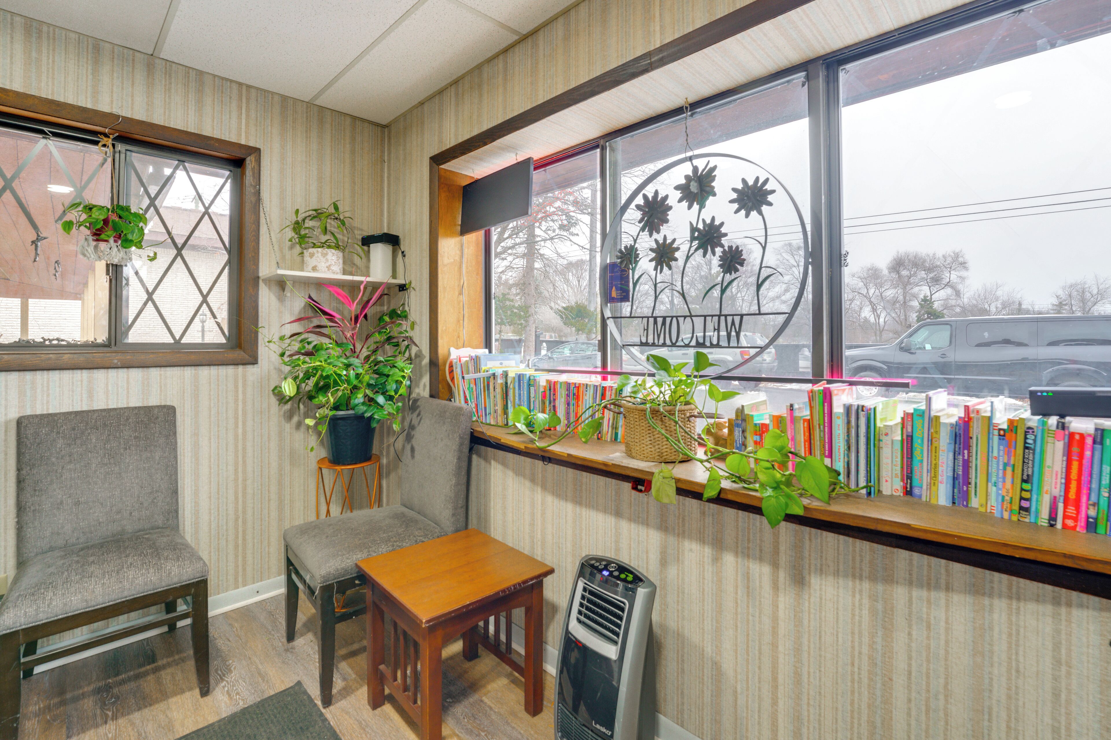 A cozy room with a wooden table, a chair, a bookshelf filled with books, and a window with a view of the street.