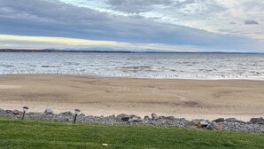 A beach with a rocky shoreline and a grassy foreground. - Stunning Views & Beach Access: Plattsburgh Getaway (Plattsburgh)