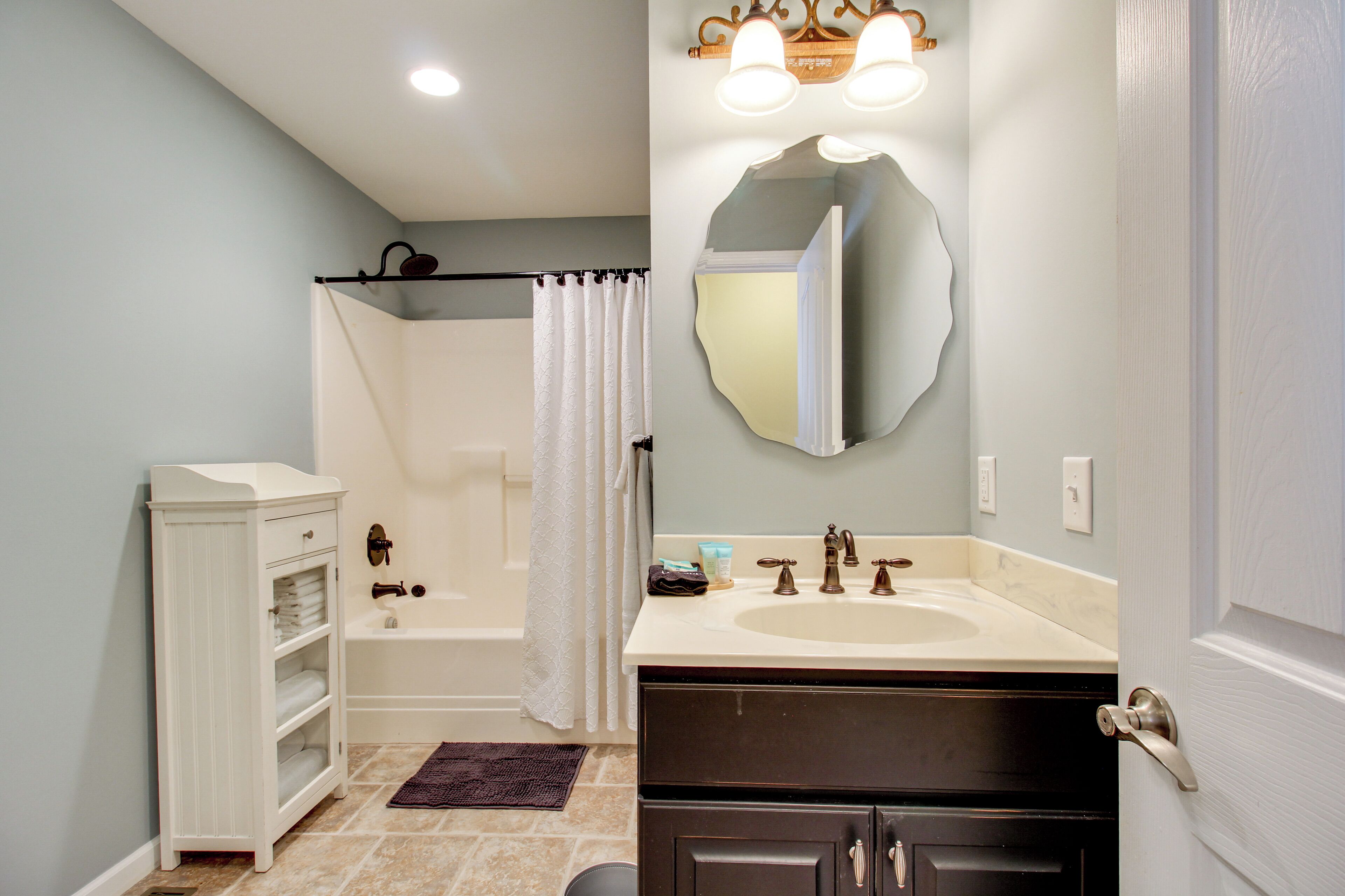 A bathroom with a bathtub, a vanity with a sink, a mirror, and a towel rack.