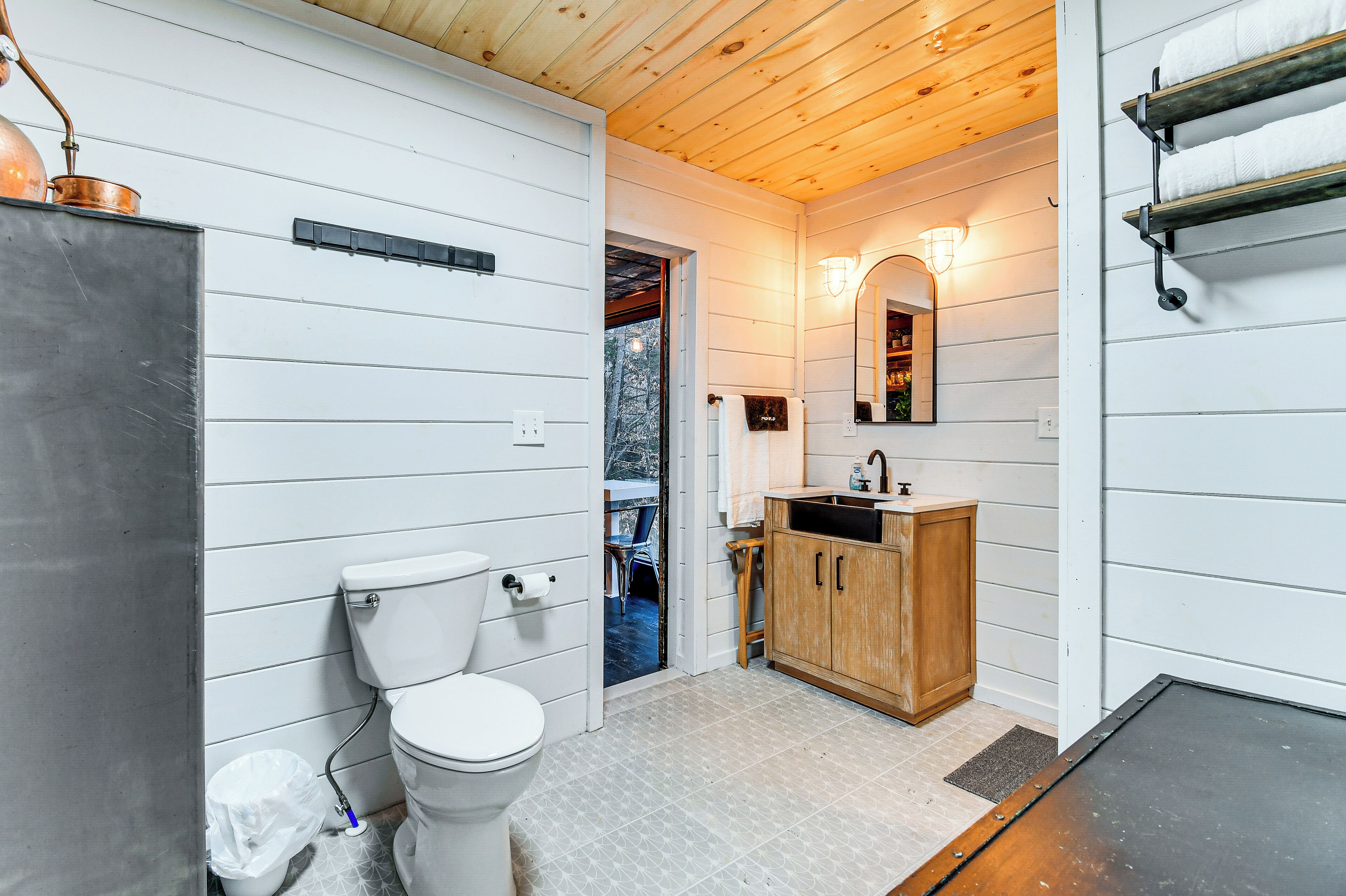 A bathroom with a white toilet, wooden cabinets, a sink, and a mirror.