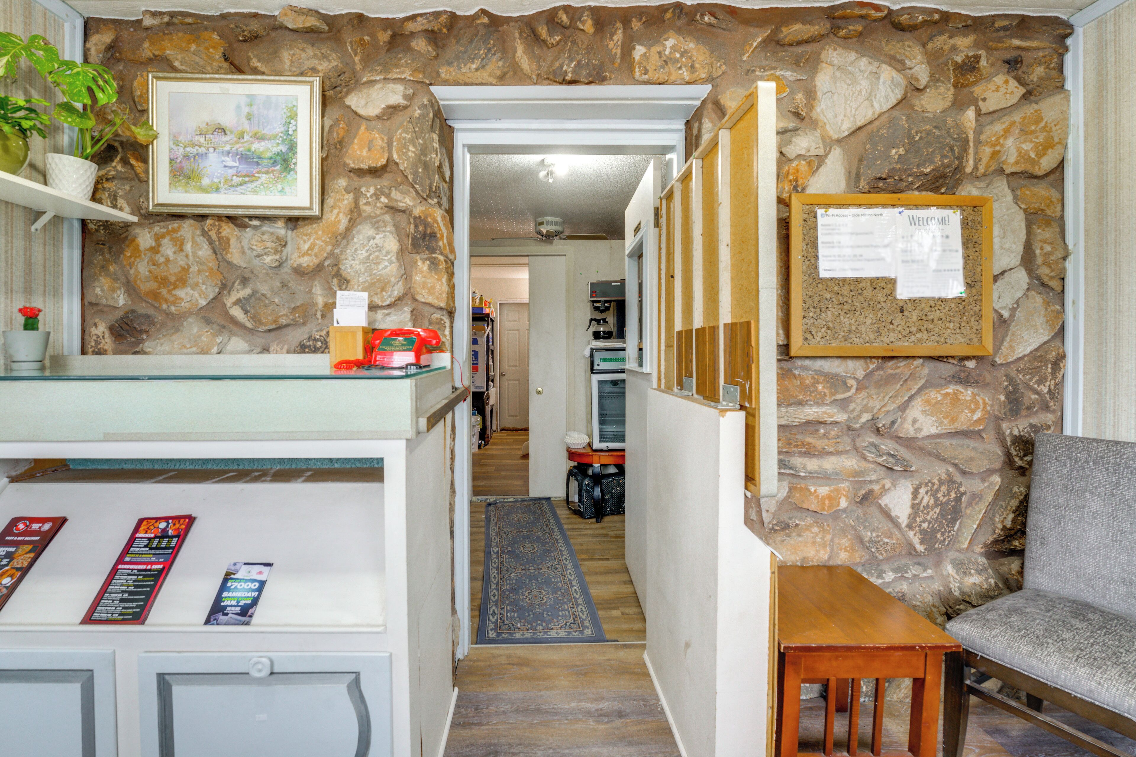 A stone-walled hallway with a reception desk, a framed welcome sign, and a grey sofa.