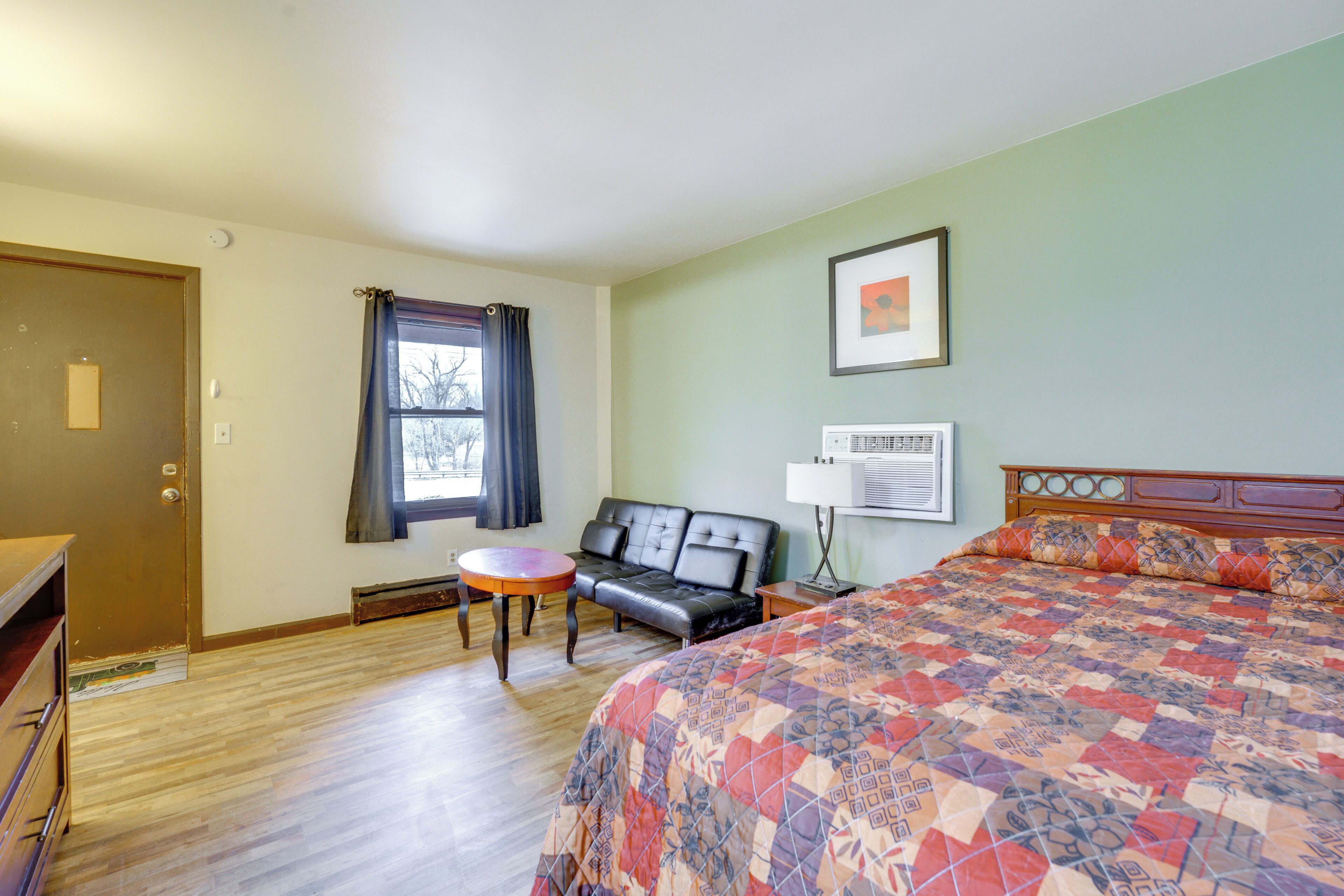 A hotel room with a bed, a sofa, a small table, and a window with curtains.