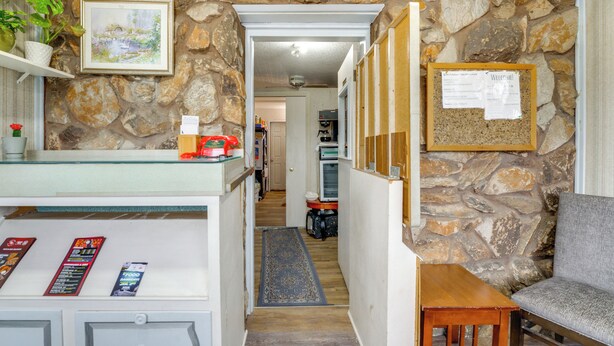 A stone-walled hallway with a reception desk, a framed welcome sign, and a grey sofa. - Slopes-ready Studio Near Pine Knob (Clarkston)