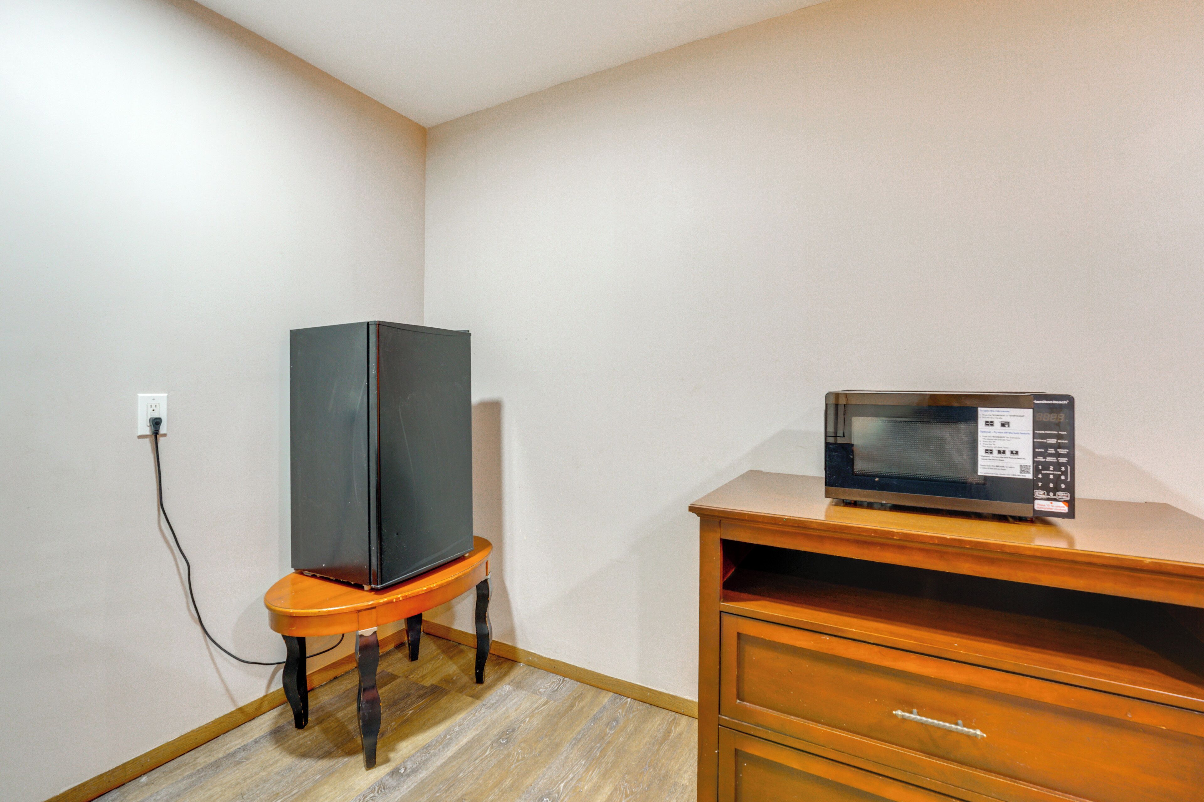 A small room with a wooden dresser, a television on a stand, and a microwave on top of the dresser.