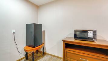 A small room with a wooden dresser, a television on a stand, and a microwave on top of the dresser.
