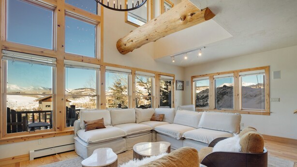 Ein geräumiges Wohnzimmer mit einer großen Eckcouch, einem Couchtisch und einem Kamin. Große Fenster bieten Blick auf eine verschneite Landschaft.
