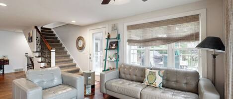 A living room with a sofa, armchair, and ottoman, a staircase, and a ceiling fan.