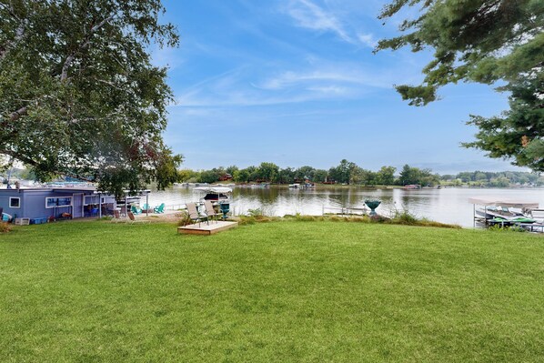 A lakeside property with a grassy lawn, a dock with boats, and a small building with a blue exterior. - Lakefront + Dock! Family-friendly Wisconsin Escape (Lodi)