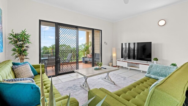 Ein modernes Wohnzimmer mit einem grünen Sofa, einem Fernseher und einer Glastür, die auf eine Terrasse im Freien führt.