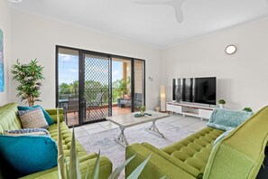 Ein modernes Wohnzimmer mit einem grünen Sofa, einem Fernseher und einer Glastür, die auf eine Terrasse im Freien führt.