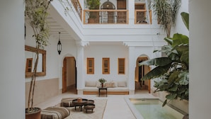 A spacious courtyard with a white wall, a wooden bench, a small table, and a potted plant. - Riad Babel (Marrakech)