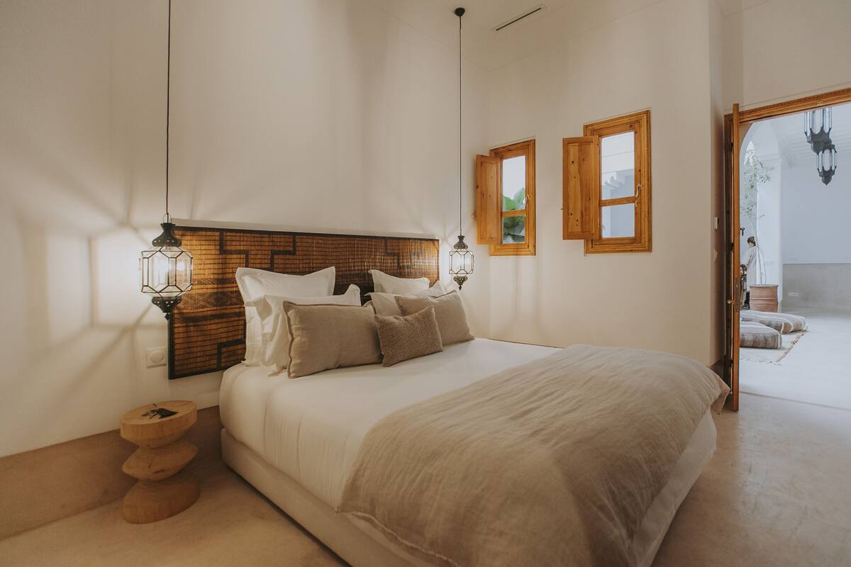 A bedroom with a large bed, wooden headboard, two windows, and a hanging light fixture.