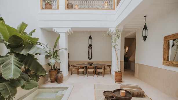 A spacious indoor area with a dining table, chairs, and a seating area with cushions. There are potted plants and a hanging light fixture. - Riad Babel (Marrakech)