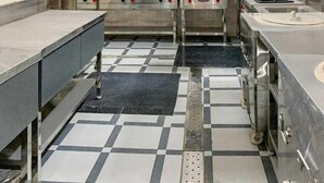 A commercial kitchen with stainless steel appliances, checkered flooring, and a central exhaust hood. - AKD HOMES (Noida)