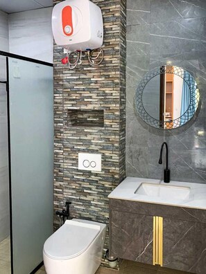 Een badkamer met een stenen muur, toilet, wastafel met een zwarte kraan en een spiegel met een ronde lijst.