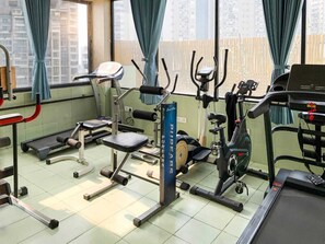 Een sportschool met diverse fitnessapparaten, waaronder loopbanden, een hometrainer en krachtapparaten.