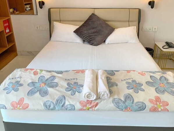 A neatly made bed with a floral bedspread and two rolled towels. - AKD HOMES (Noida)