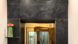 An elevator with glass doors, black marble walls, and a small shelf with a vase. - AKD HOMES (Noida)