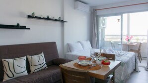 A modern hotel room with a sofa, a dining table with chairs, a balcony with a table and chairs, and a bed with white bedding. - WELCS ESTUDIO 308 EMP near the sea (Empuriabrava)
