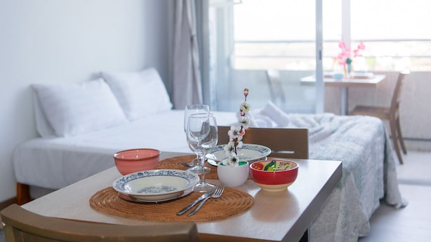 A neatly arranged dining table with plates, bowls, and cutlery in a hotel room with a bed and a view of the outdoors. - WELCS ESTUDIO 308 EMP near the sea (Empuriabrava)