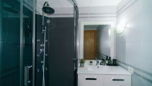 A modern bathroom with a glass shower enclosure, a white sink with toiletries, and a mirror above the sink. - WELCS ESTUDIO 308 EMP near the sea (Empuriabrava)