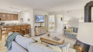 A modern living room with a fireplace, a dining area with wooden furniture, and a TV mounted on the wall. - Freshly Updated Condo, Across The Street From The Resort Edel O 2 Bedroom Apts (Park City)